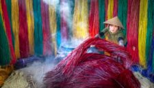 Seorang penenun perempuan di Sumba Timur sedang memintal benang kapas tradisional menggunakan alat tenun kayu non-mesin di pelataran rumah adat. Proses pembuatan kain tenun ini memanfaatkan pewarna alami dari tumbuhan lokal yang membutuhkan waktu pengerjaan hingga bertahun-tahun.