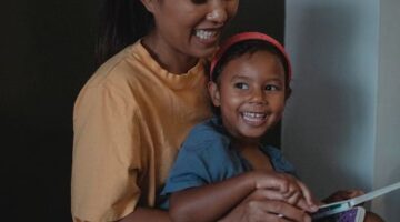 Momen hangat seorang ibu yang membacakan buku cerita rakyat Nusantara kepada buah hatinya sebelum tidur untuk melatih imajinasi dan memperkuat ikatan emosional keluarga.
