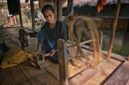 Seorang perempuan perajin di Sumba Timur memintal benang menggunakan alat tenun kayu tradisional di pekarangan rumah adatnya.