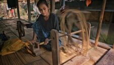Seorang perempuan perajin di Sumba Timur memintal benang menggunakan alat tenun kayu tradisional di pekarangan rumah adatnya.