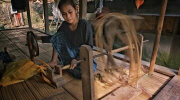 Seorang perempuan perajin di Sumba Timur memintal benang menggunakan alat tenun kayu tradisional di pekarangan rumah adatnya.